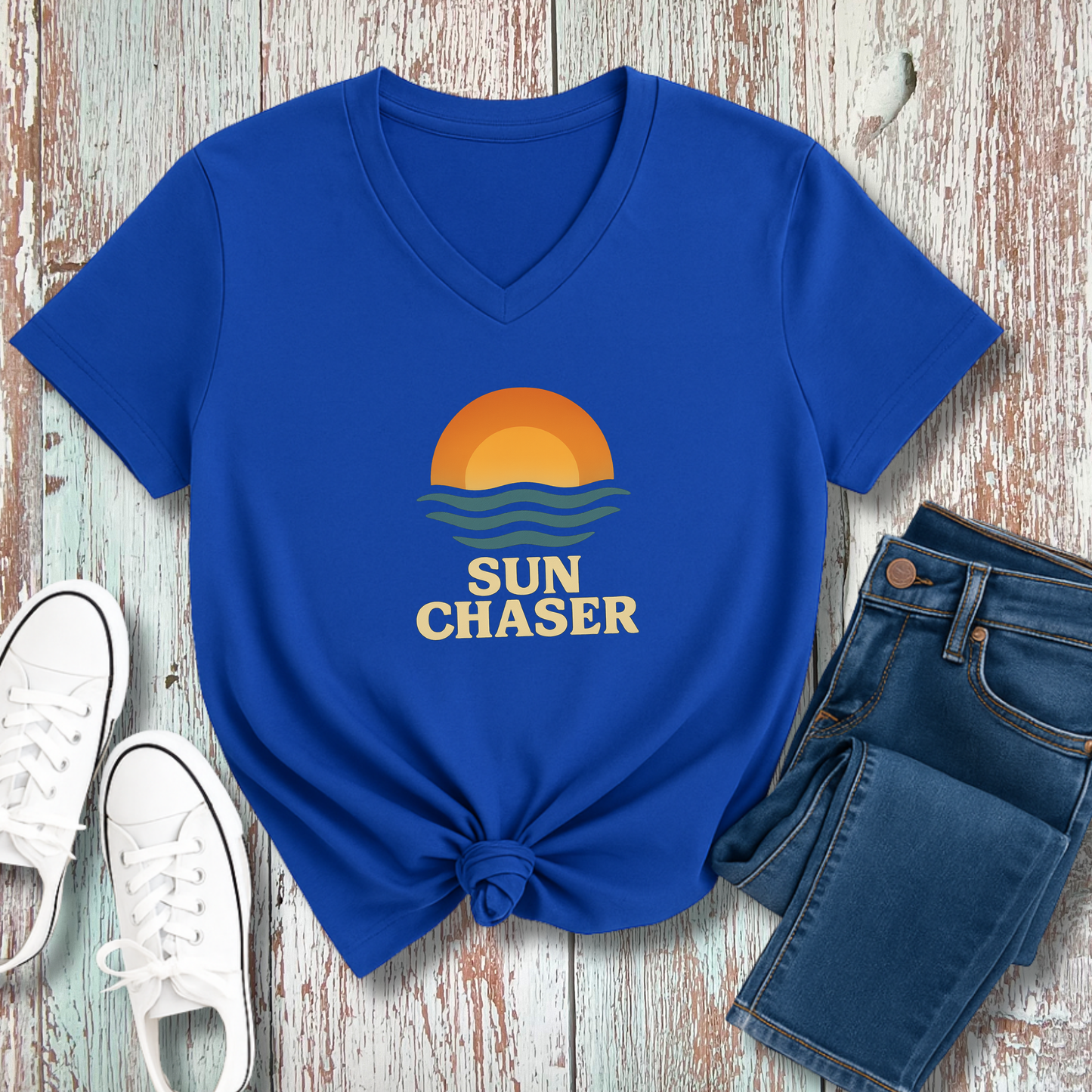 Blue t-shirt with 'Sun Chaser' design on a wooden surface with jeans and sneakers.
