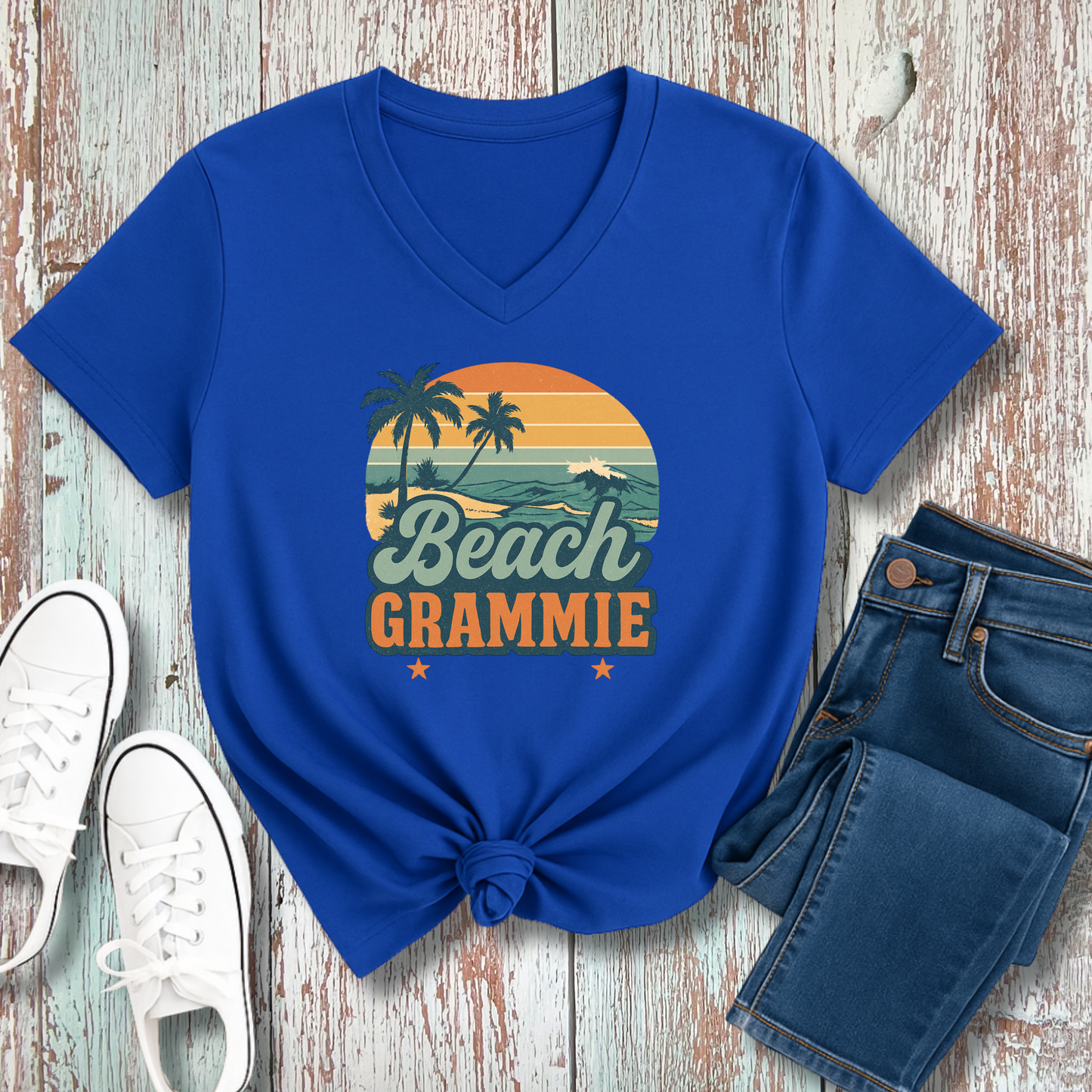 Blue t-shirt with 'Beach Grammie' design on a wooden surface with jeans and sneakers.