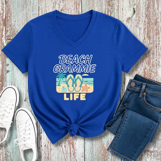 Blue t-shirt with 'Beach Grammie Life' design on a wooden surface with jeans and sneakers.