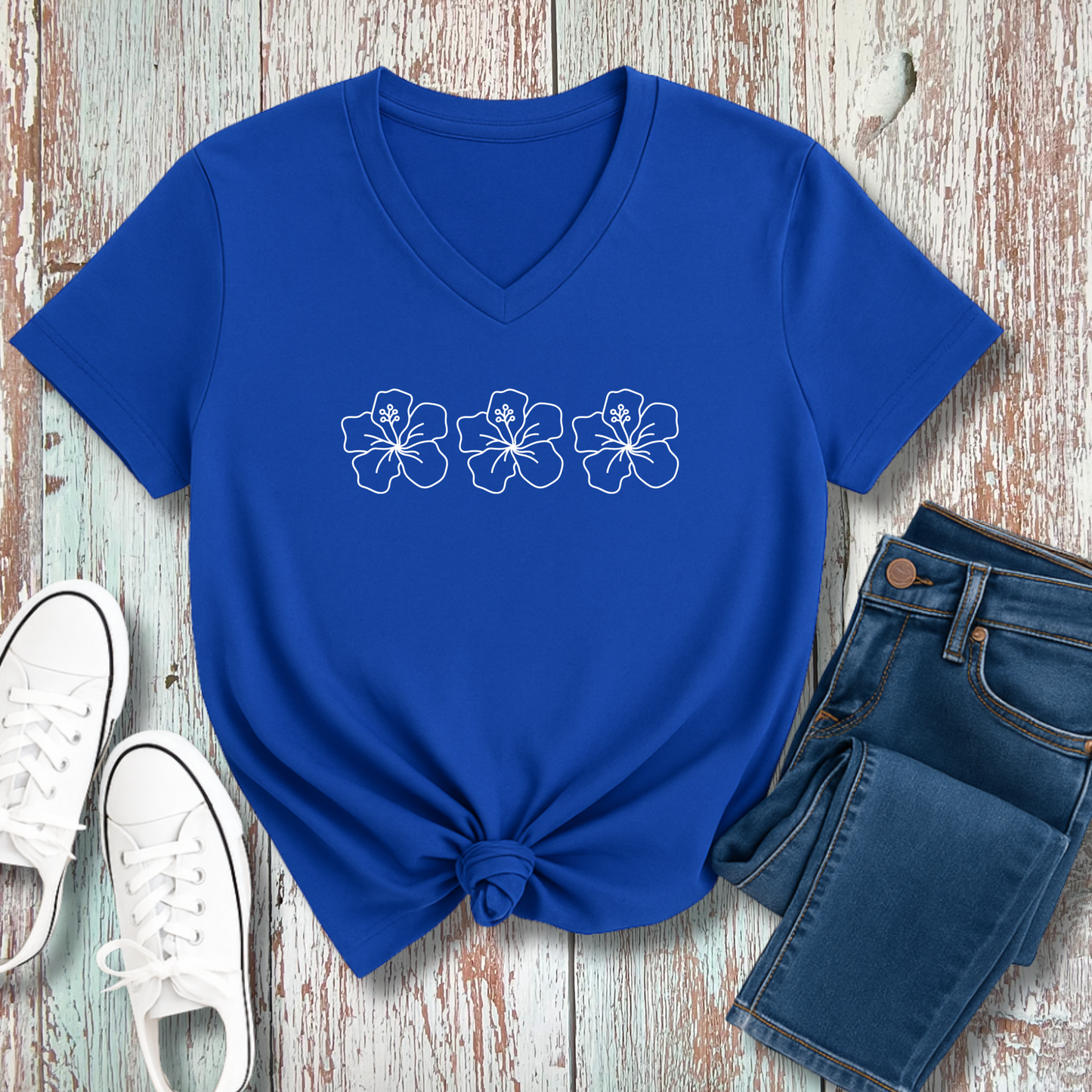 Blue t-shirt with floral designs on a wooden surface with jeans and sneakers.