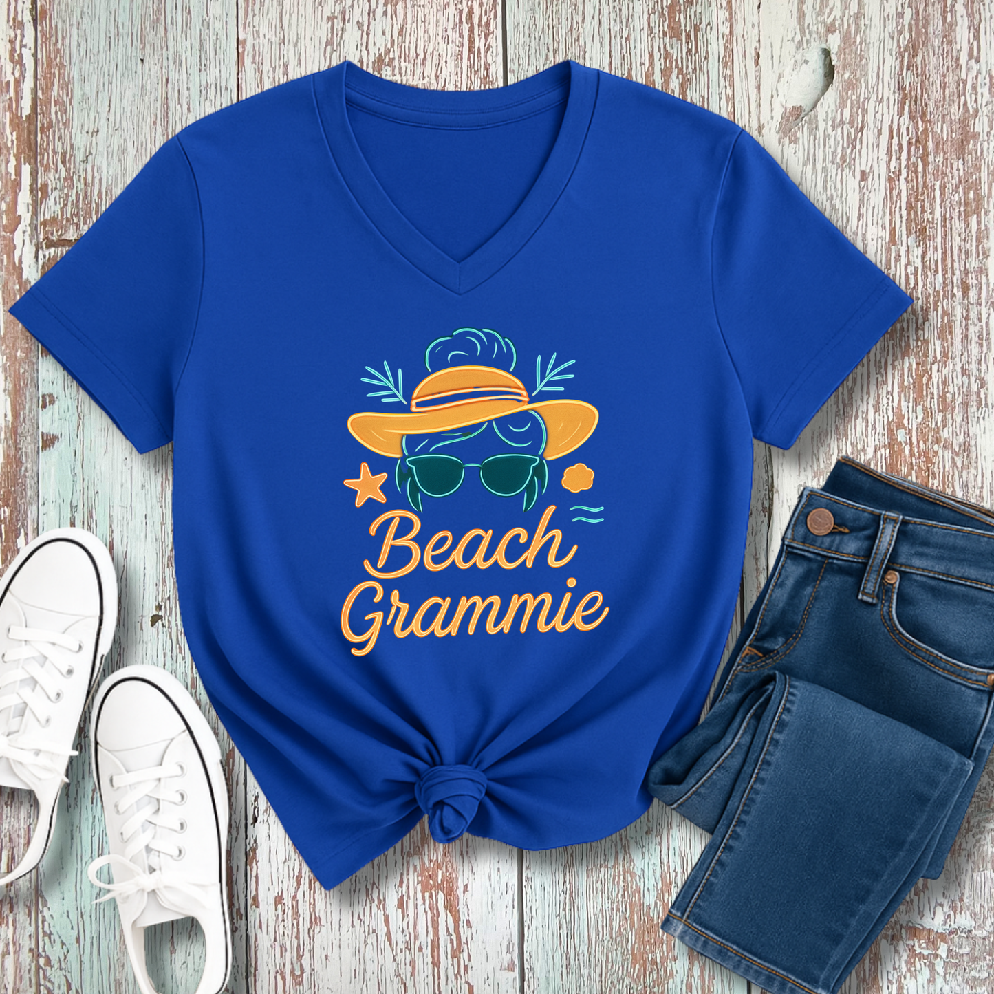 Blue t-shirt with 'Beach Grammie' design on a wooden surface with jeans and sneakers.