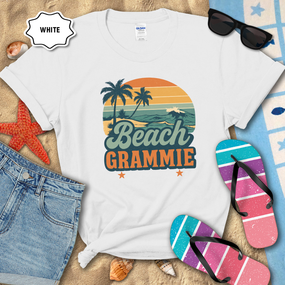 White t-shirt with 'Beach Grammie' design on sand with flip-flops and sunglasses.