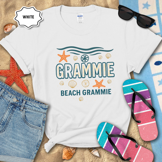 White t-shirt with 'GRAMMIE BEACH GRAMMIE' text and beach-themed graphics on a sandy background with flip-flops and sunglasses.