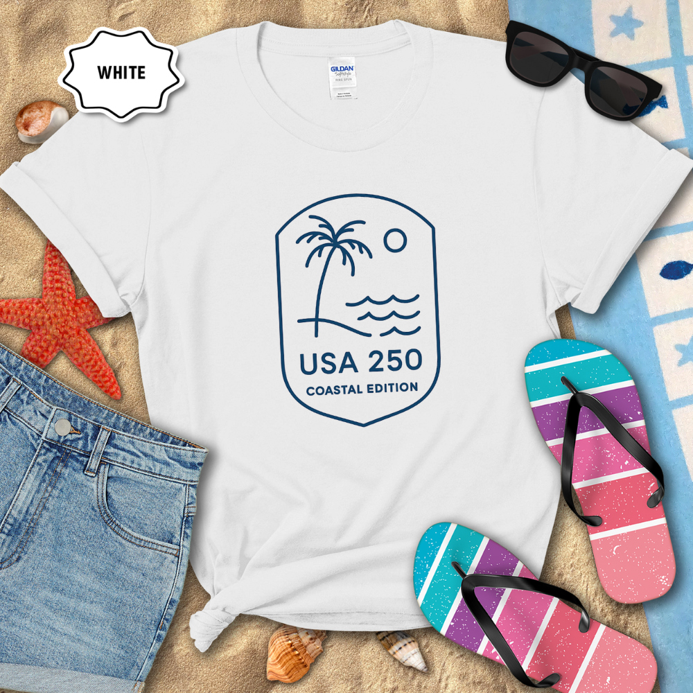 White t-shirt with a palm tree and wave design, sunglasses, and flip-flops on a beach setting.