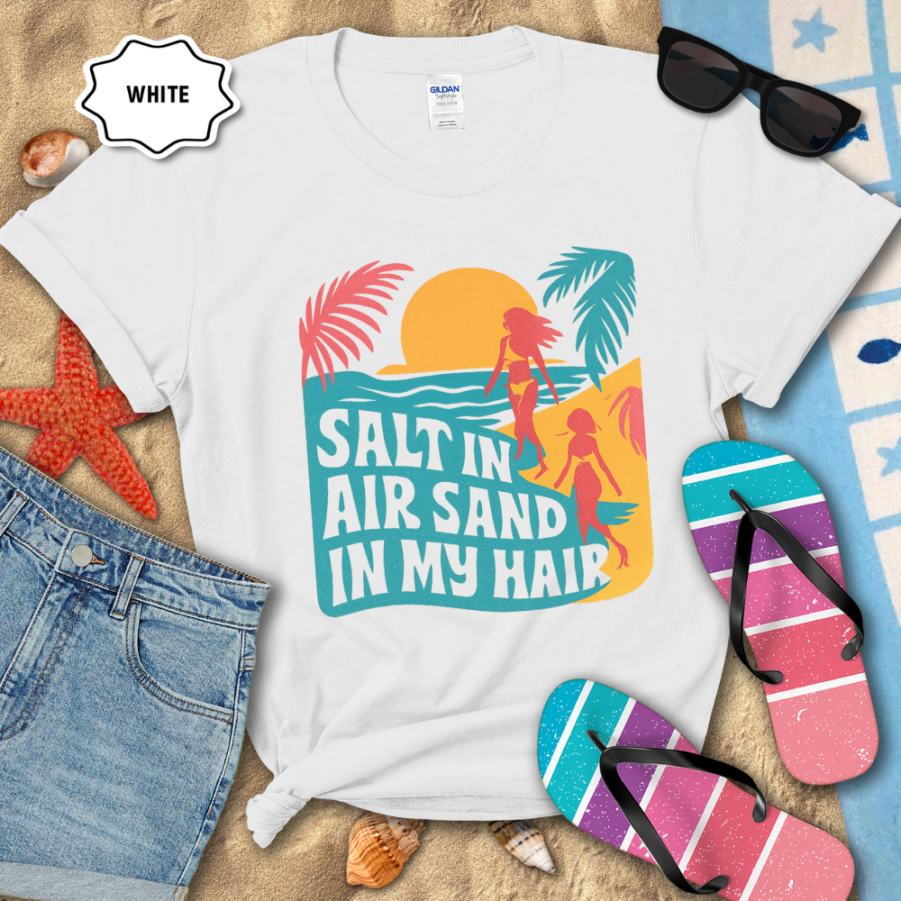White t-shirt with beach-themed design and accessories on sand