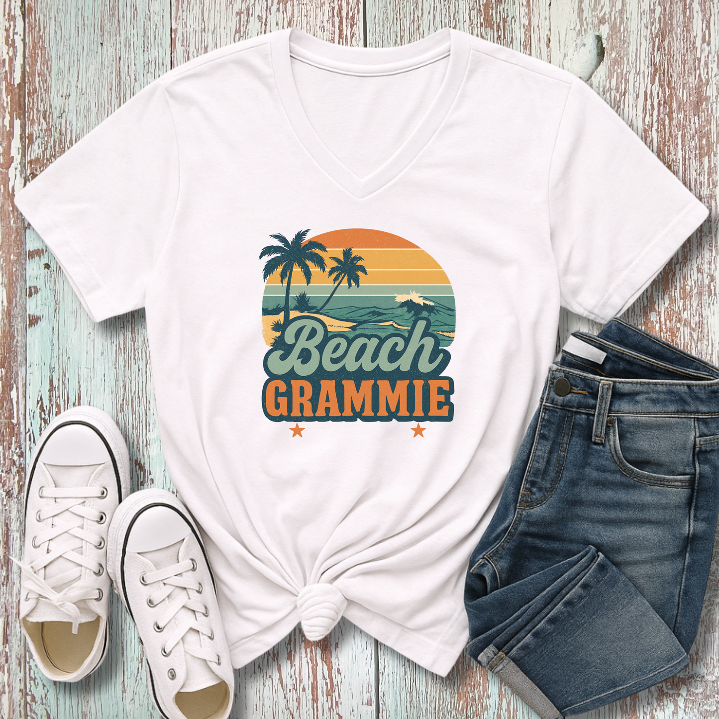 White t-shirt with 'Beach Grammie' design, white sneakers, and blue jeans on a wooden surface
