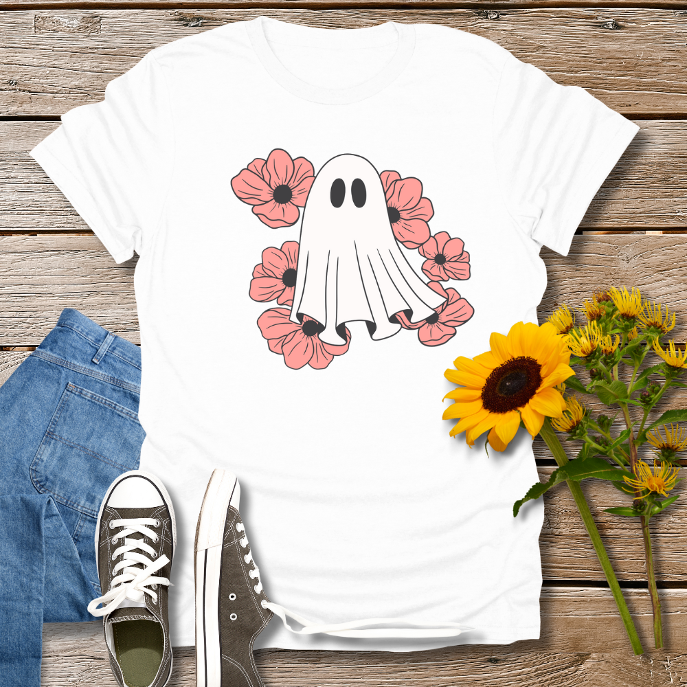 White t-shirt with ghost and flower design on a wooden surface with jeans and sunflowers.