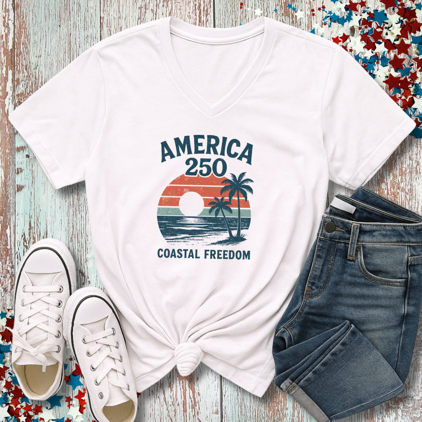 White t-shirt with 'America 250 Coastal Freedom' design, paired with white sneakers and blue jeans on a wooden surface.
