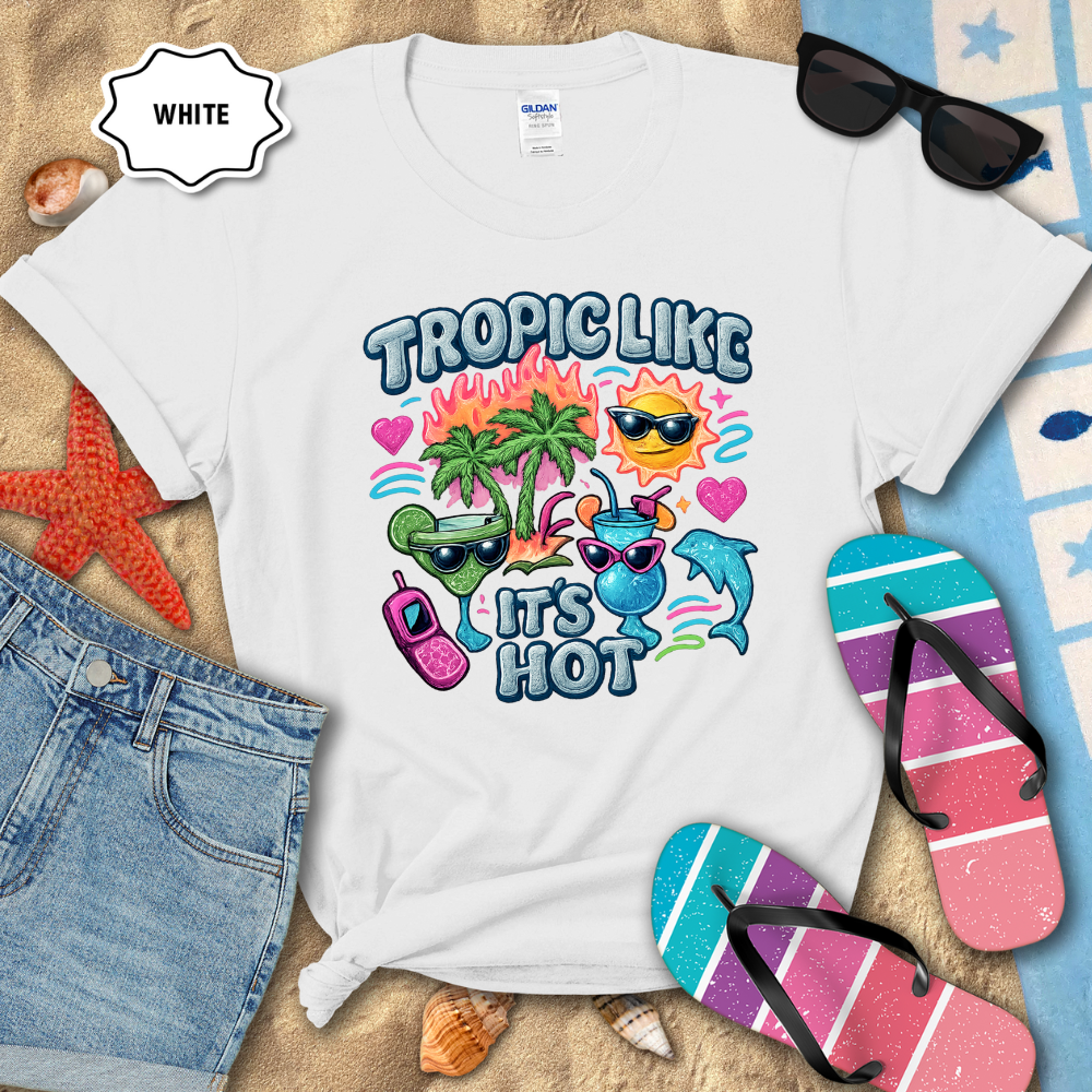 White t-shirt with tropical-themed design on a sandy background with flip-flops and sunglasses.