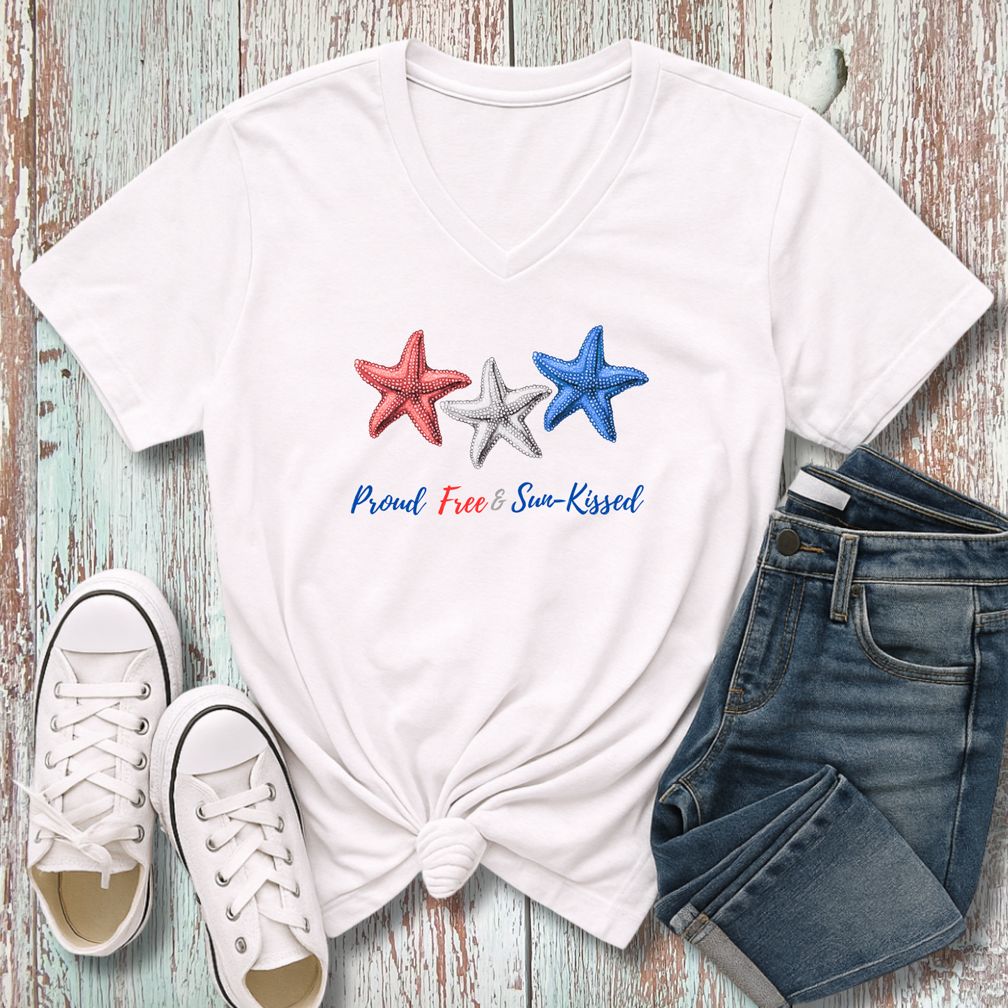 White t-shirt with star designs and text, paired with white sneakers and denim shorts on a wooden surface.