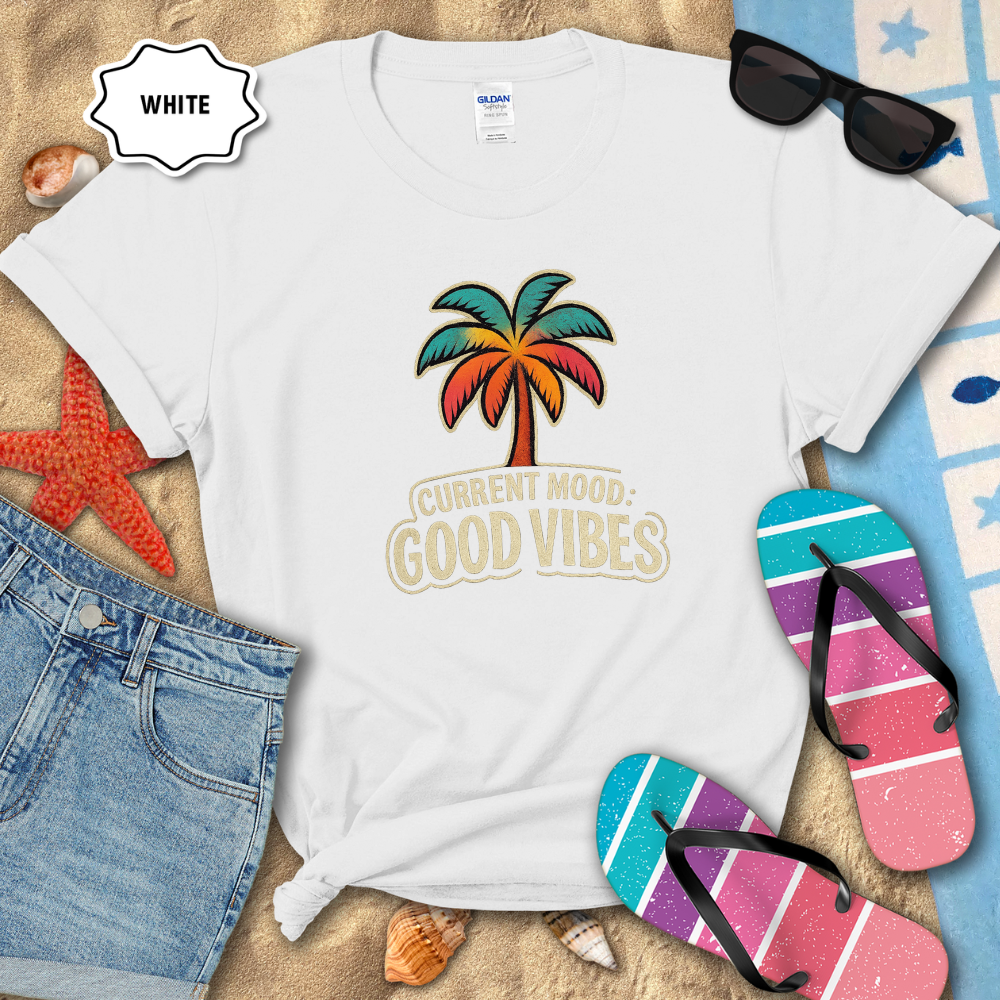 White t-shirt with palm tree and 'Current Mood: Good Vibes' text on a beach-themed background with sunglasses, flip-flops, and denim shorts.