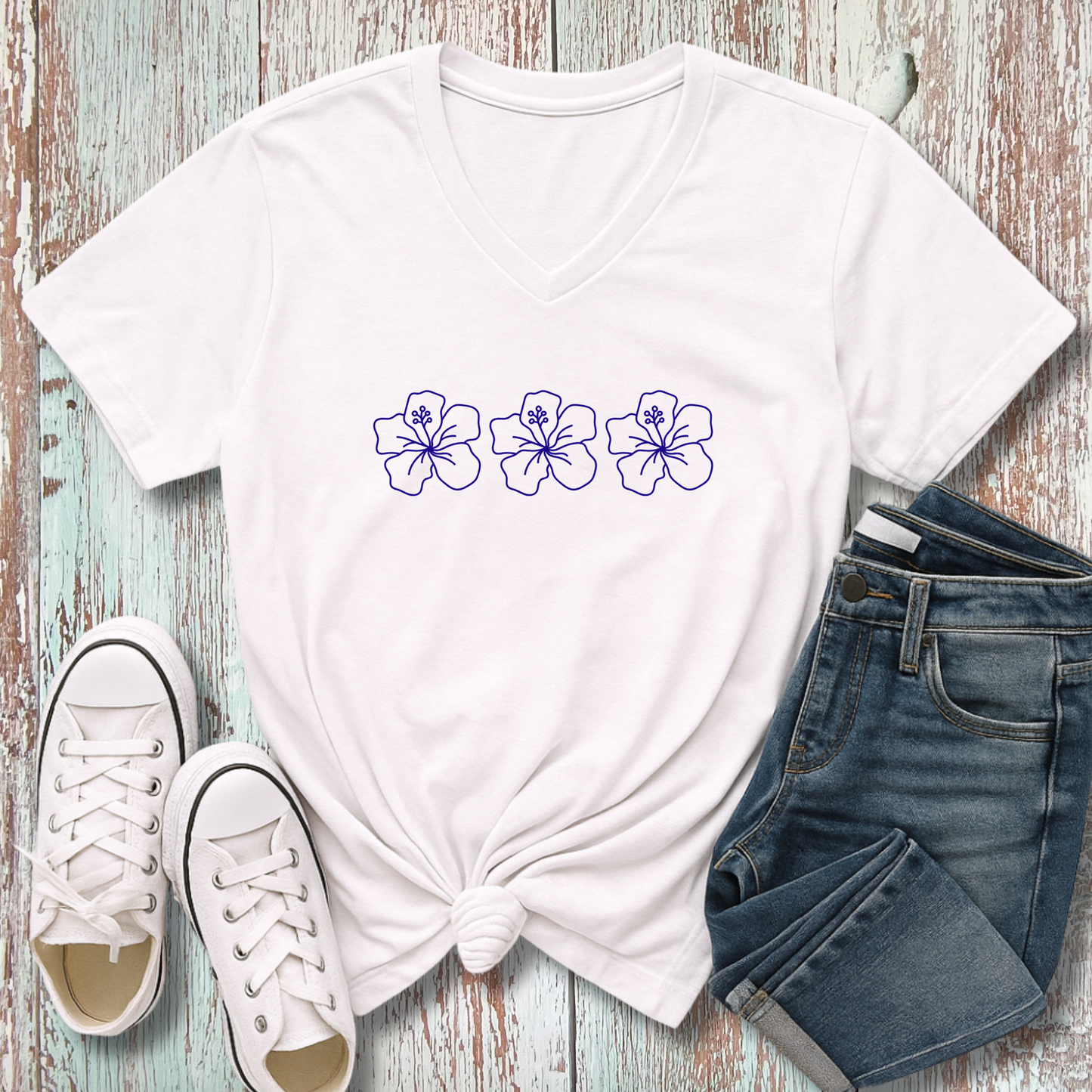 White t-shirt with floral designs, white sneakers, and blue jeans on a wooden surface