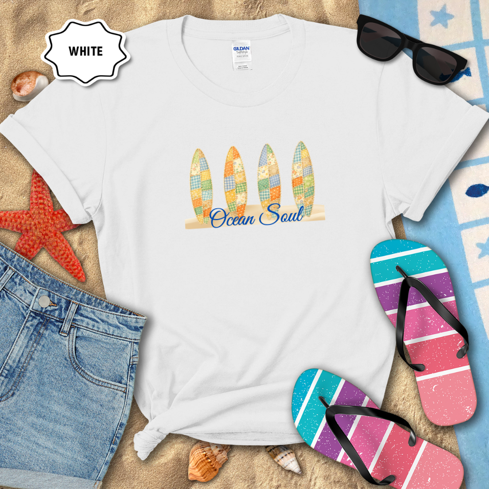 White t-shirt with a colorful turtle design and 'Sloppy Coastal Days' text, placed on sand with beach accessories.