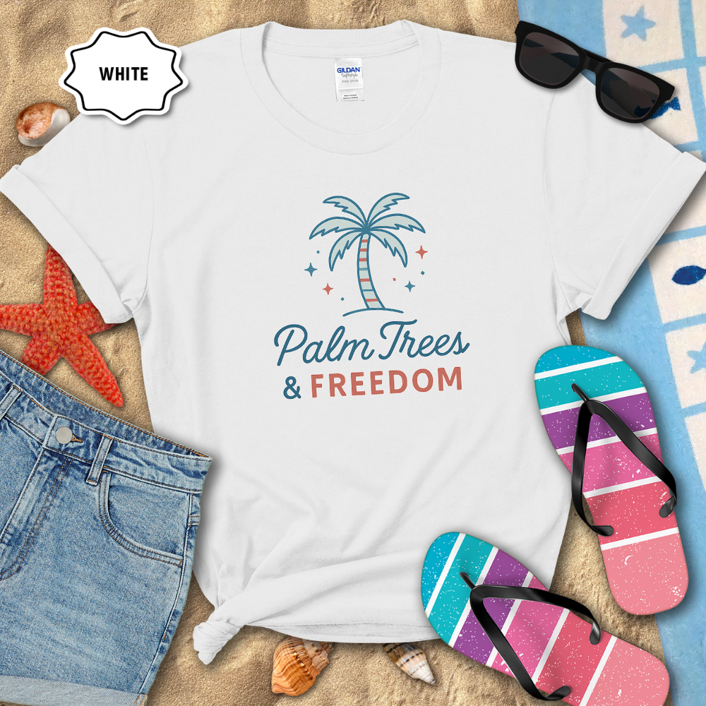 White t-shirt with 'Palm Trees & Freedom' design on a sandy background with flip-flops and sunglasses.