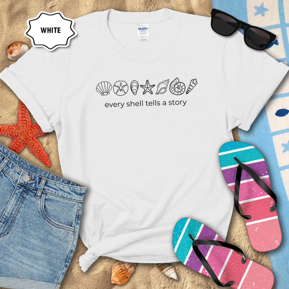 White t-shirt with fish illustrations and 'Unity in Diversity' text on a beach setting with sunglasses, flip-flops, and denim shorts.