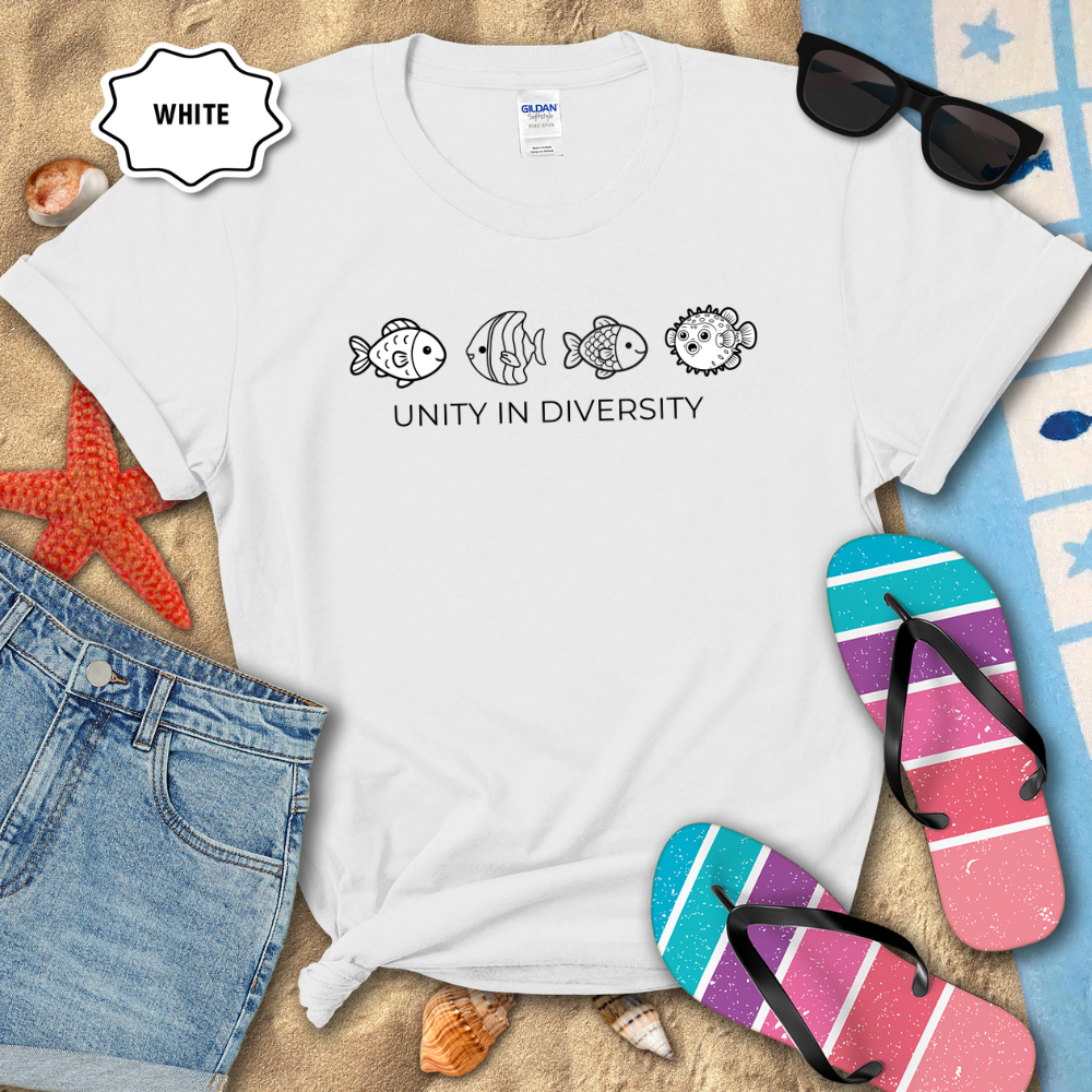 White t-shirt with fish illustrations and 'Unity in Diversity' text on a beach setting with sunglasses, flip-flops, and denim shorts.