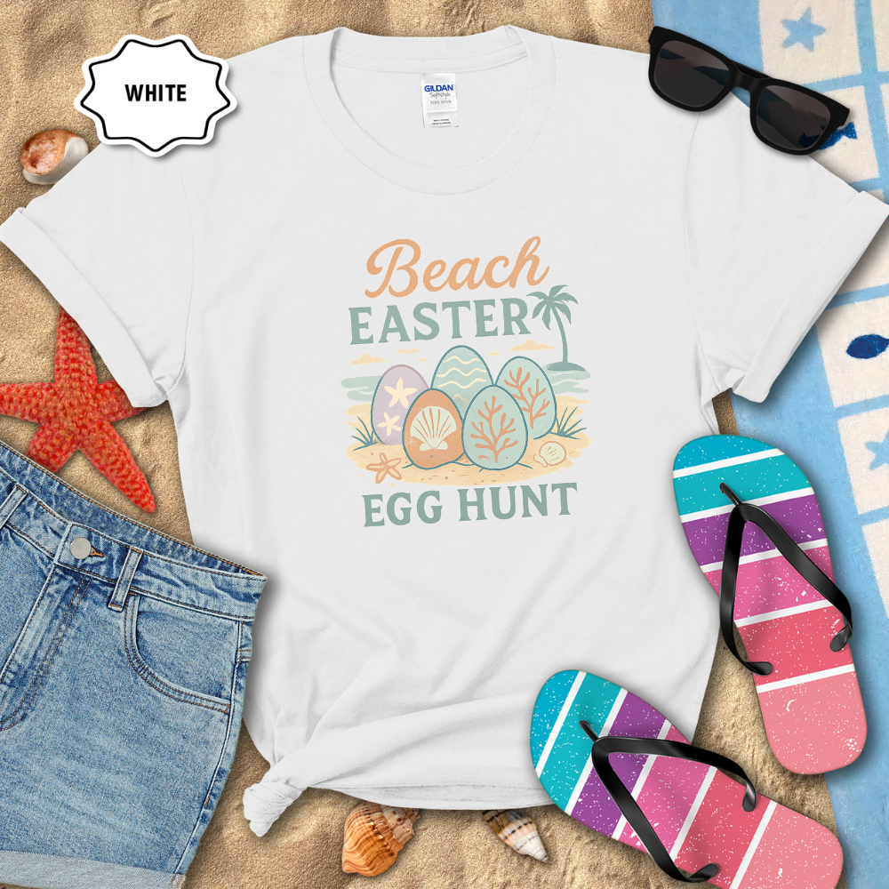 White t-shirt with 'Beach Easter Egg Hunt' design on sand with flip-flops and sunglasses.