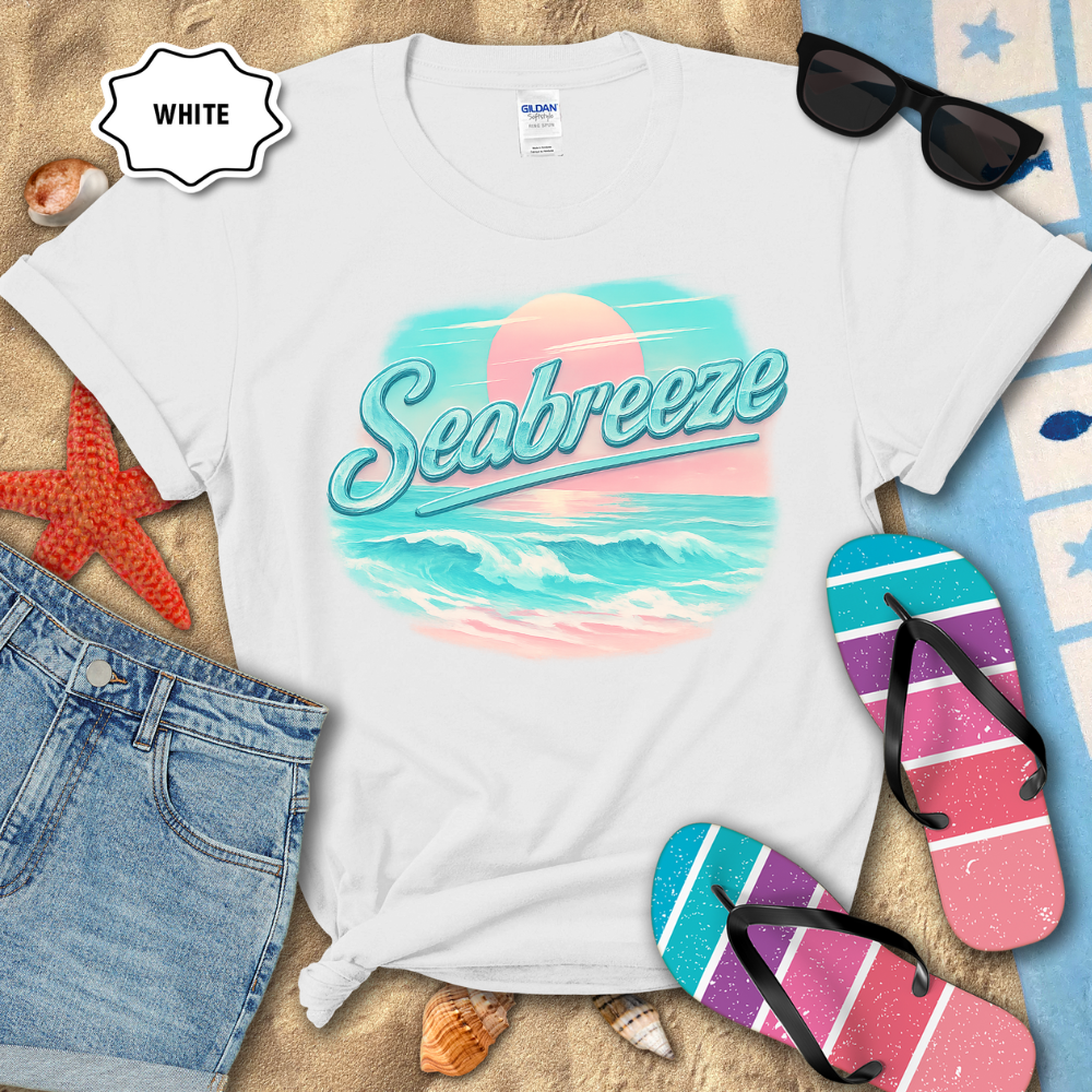 White t-shirt with 'Seabreeze' design on a sandy surface with beach accessories.