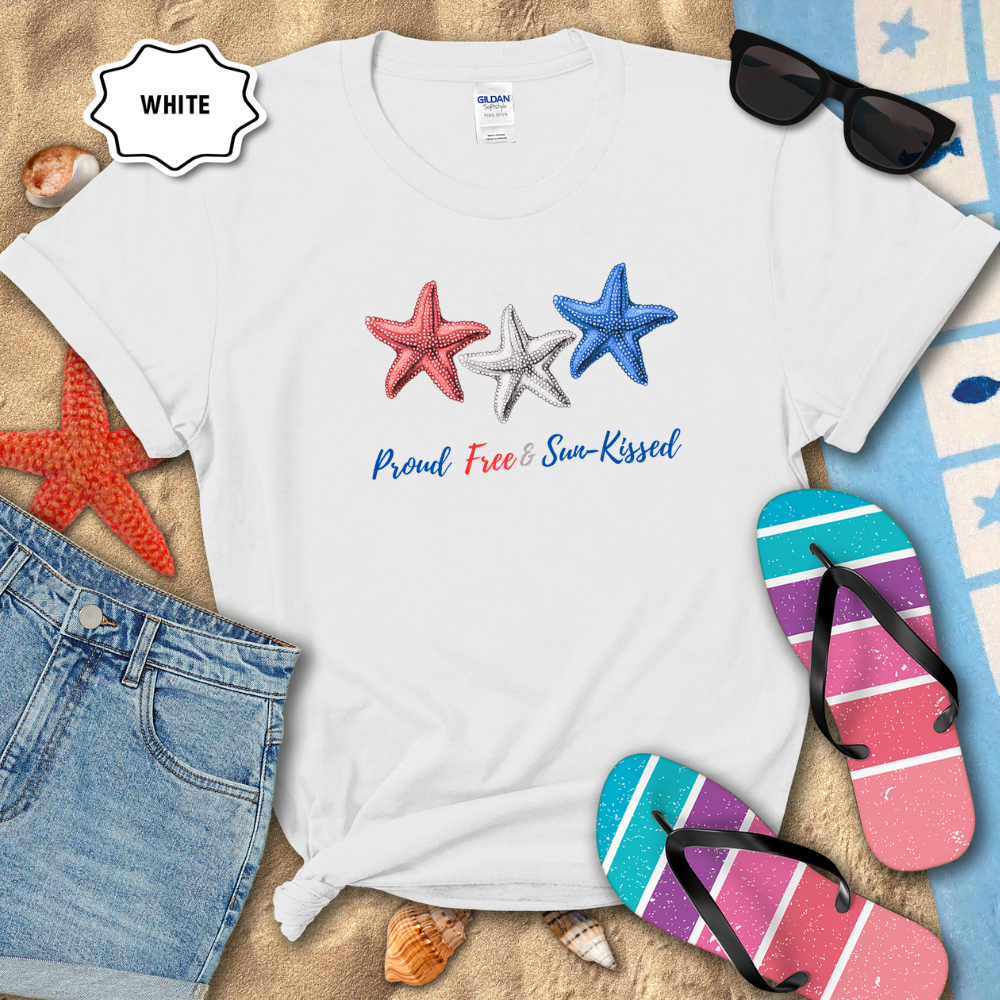 White t-shirt with star designs and text on a sandy background with flip-flops and sunglasses.