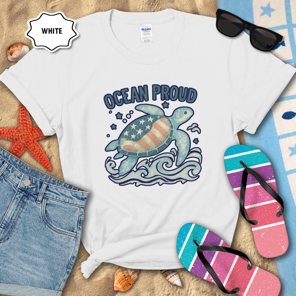 White t-shirt with ocean-themed design featuring a turtle and American flag, surrounded by beach accessories.