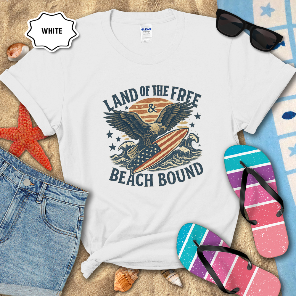 White t-shirt with 'Coastal Freedom Beach Co' design on sand with sunglasses and flip-flops.