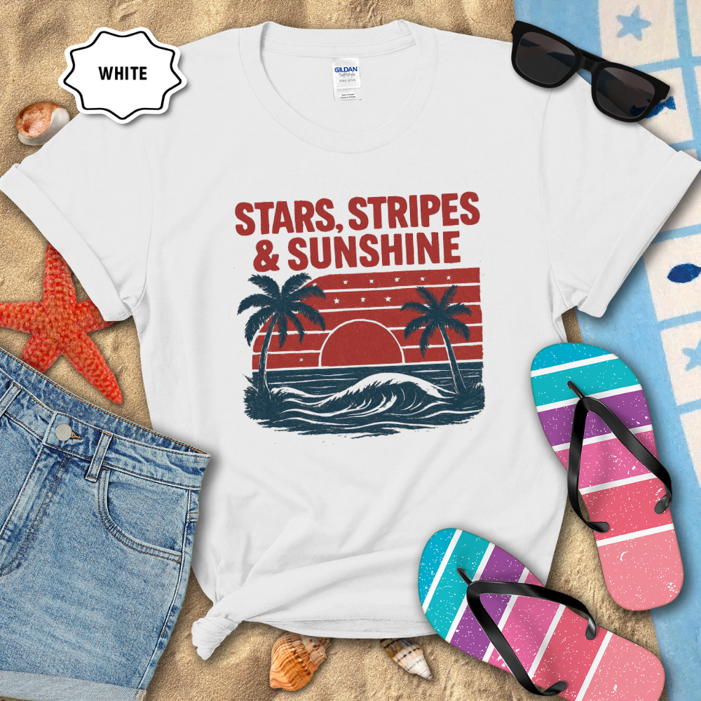 White t-shirt with 'Stars, Stripes & Sunshine' design on a sandy background with flip-flops and sunglasses.