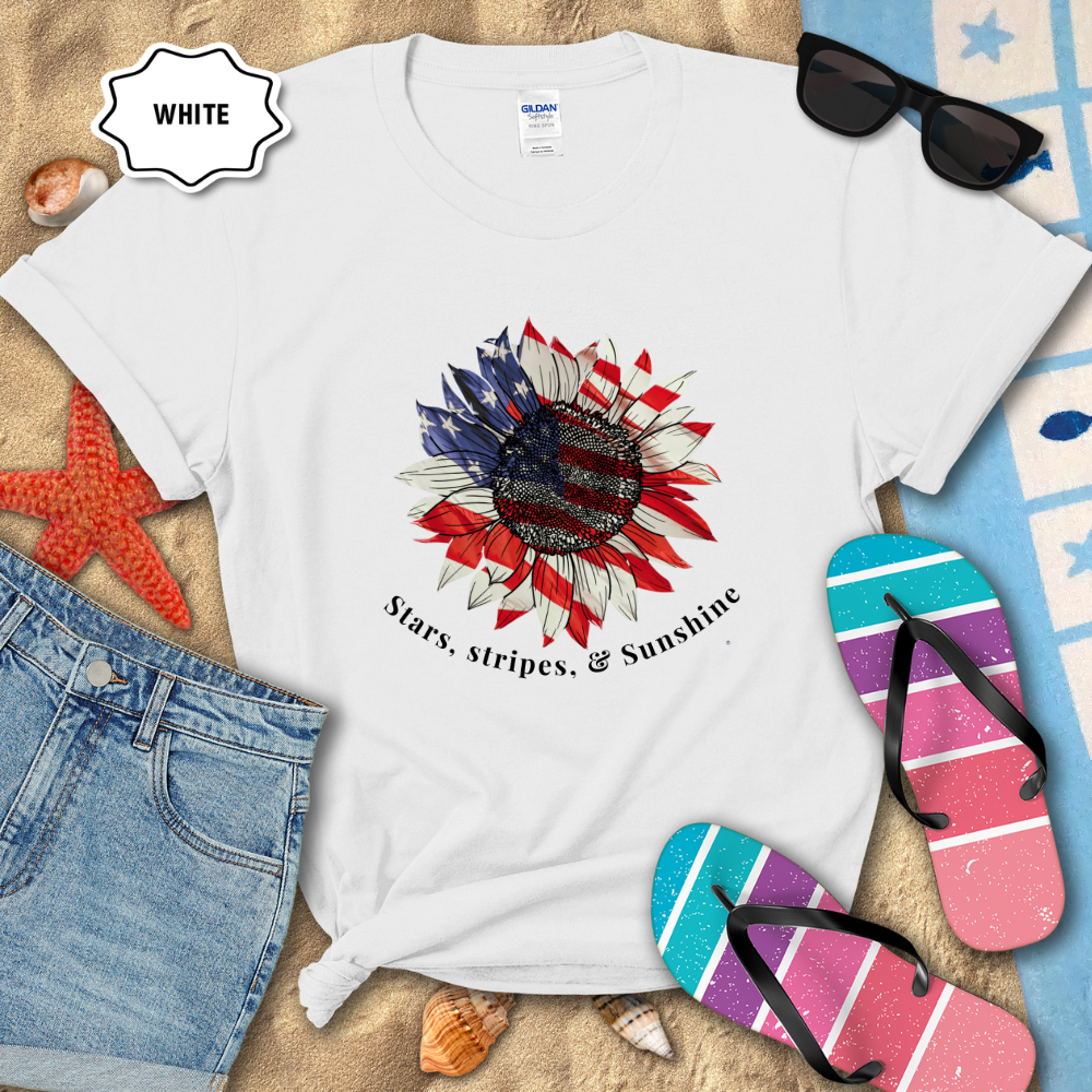 White t-shirt with a sunflower design and text on a sandy background with flip-flops and sunglasses.