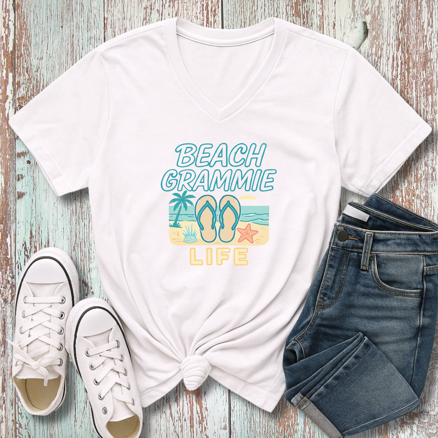 White t-shirt with 'Beach Grammie Life' design, white sneakers, and blue jeans on a wooden surface.