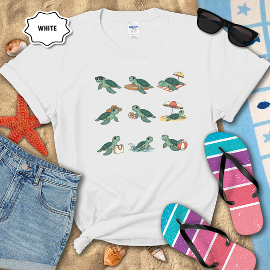 White t-shirt with turtle illustrations on a sandy background with beach accessories.
