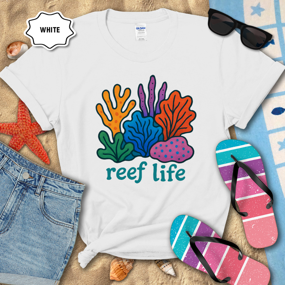 White t-shirt with 'reef life' design on a sandy surface with beach accessories.