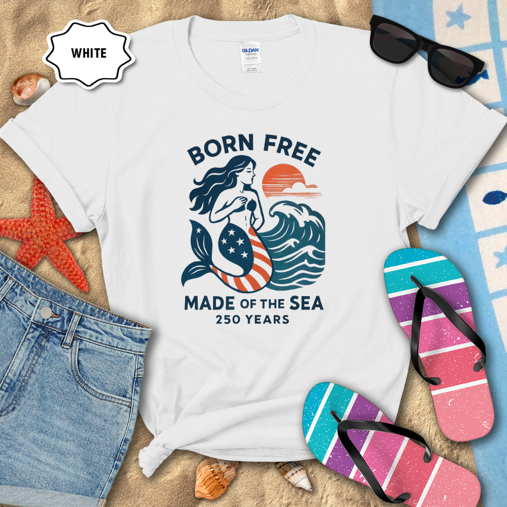 White t-shirt with mermaid graphic and text on a sandy background with flip-flops and sunglasses.